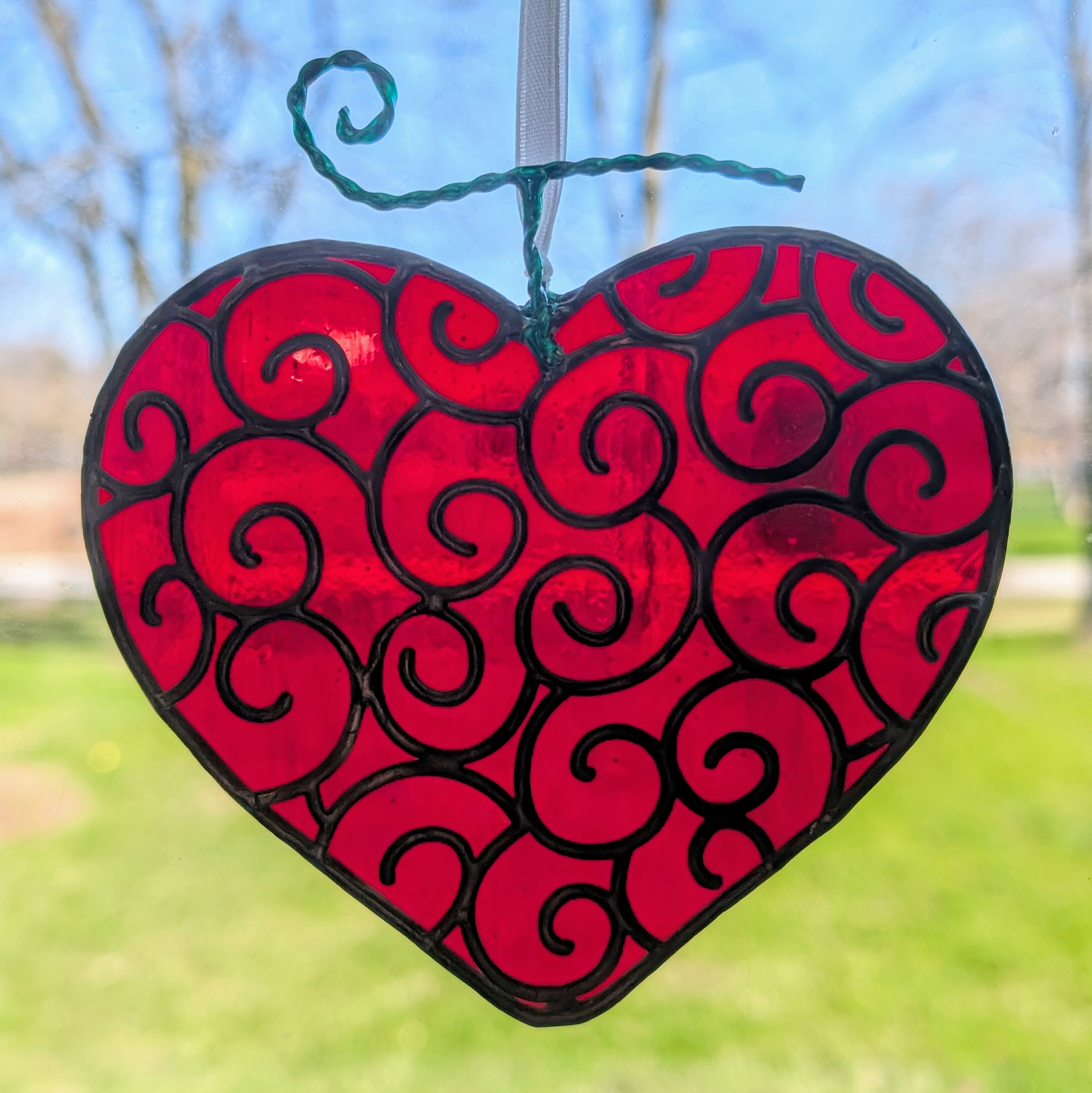 A red stained glass heart with lots of swirls on it